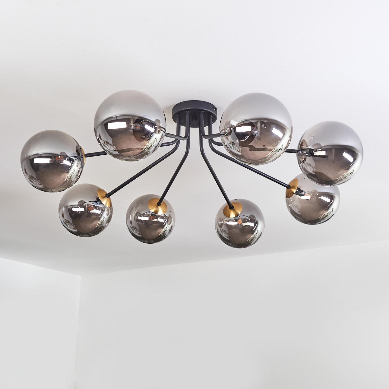 Eine moderne Deckenleuchte mit acht verspiegelten Glaskugeln, befestigt an schwarzen Armen mit goldenen Akzenten, an einer weißen Decke.
