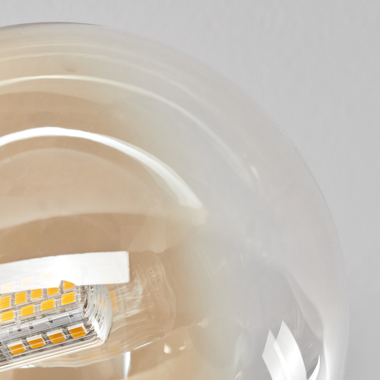 Nahaufnahme einer Glühbirne. Die Birne ist transparent mit einer gelben LED im Inneren. Der Hintergrund ist weiß.