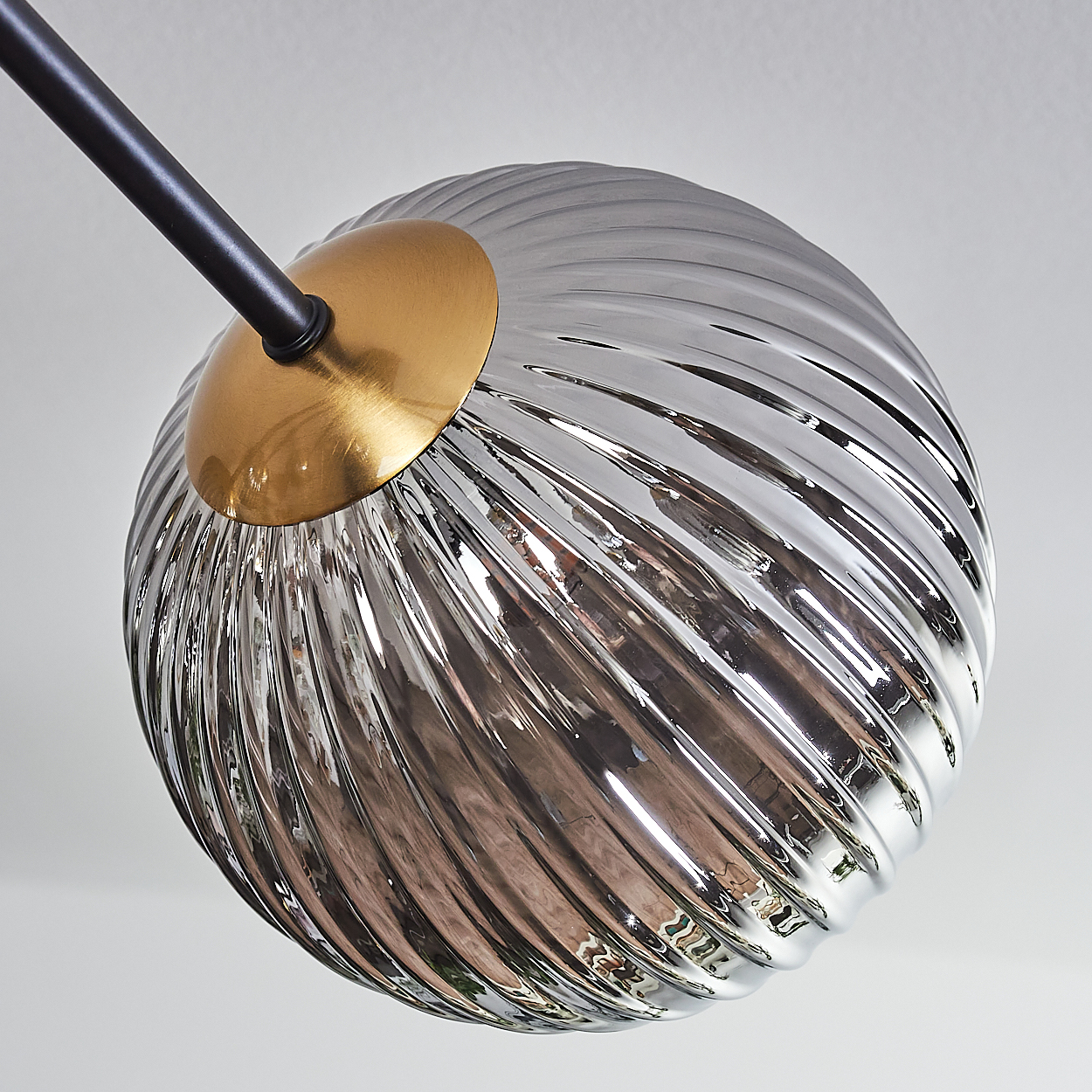 Nahaufnahme einer modernen Leuchte. Ein kugelförmiger, geriffelter Glasschirm ist an einem schwarzen Arm befestigt.