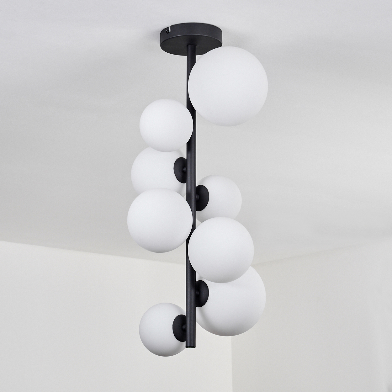 Eine schwarze, moderne Deckenleuchte mit neun weißen Kugelleuchten hängt von einer weißen Decke. Die Leuchte ist zentriert.