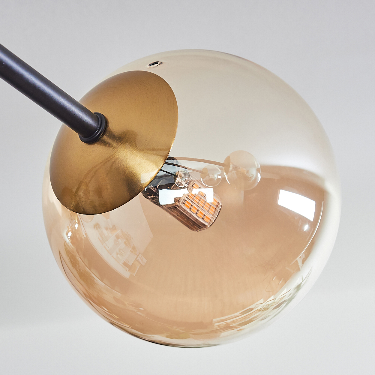 Nahaufnahme einer Leuchte. Ein kugelförmiger Glasschirm hat einen goldbraunen Farbton. Eine schwarze Stange und ein goldener Sockel tragen die Glühbirne.