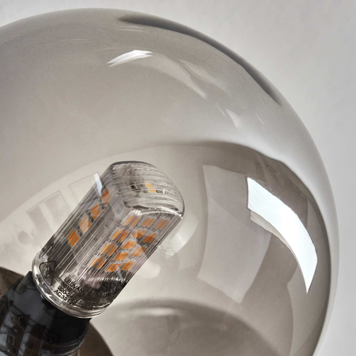 Nahaufnahme einer Glühbirne. Eine klare, zylindrische Lichtquelle befindet sich in einem grauen, kugelförmigen Glas. Der Hintergrund ist weiß.