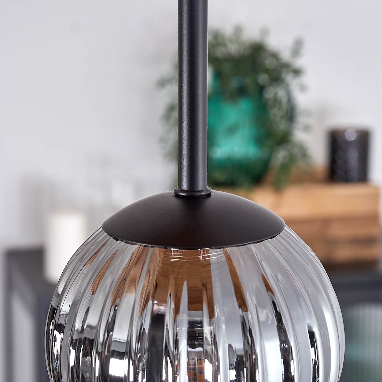 Eine geriffelte Glas-Pendelleuchte hängt herunter. Eine dunkle Metallstange und ein Schirm sind befestigt. Hintergrund hat eine grüne Vase und Holzkiste.