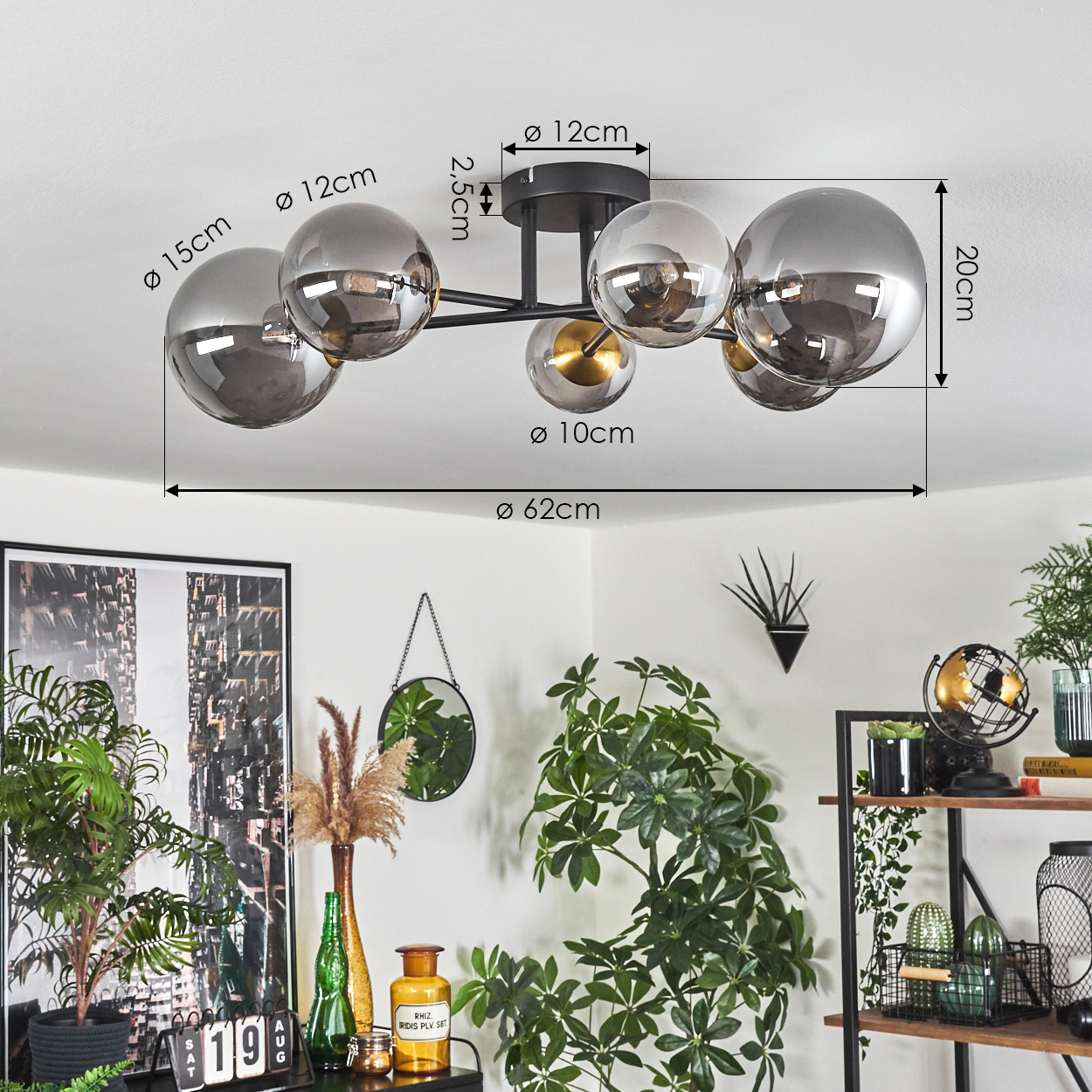 Eine moderne Deckenleuchte mit mehreren grauen Glaskugeln hängt über einem Raum mit Pflanzen, Dekoration und einem schwarzen Kunstwerk.