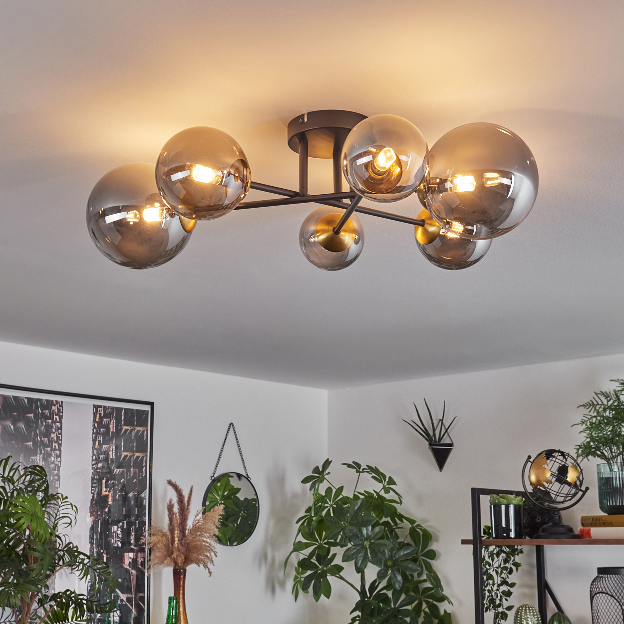 Eine moderne Deckenleuchte mit Glaskugeln und ein Rauminneres mit Pflanzen, einem Spiegel und einer Globusdekoration im Hintergrund.