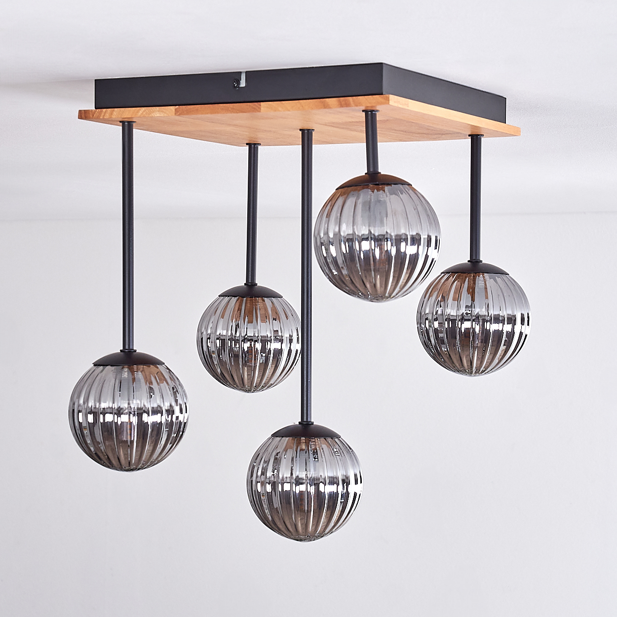 Eine moderne Deckenleuchte. Sie hat einen Holzsockel, schwarze Metallstangen und fünf silberne, gerippte Glaskugelleuchten.