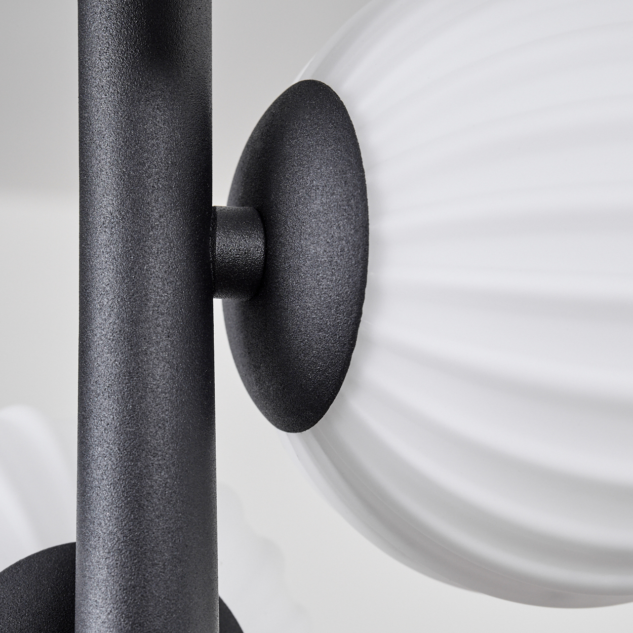 Nahaufnahme einer modernen Lampe. Sie hat einen schwarzen Metallrahmen und einen weißen, gerippten Glaskolben. Der Hintergrund ist weiß.