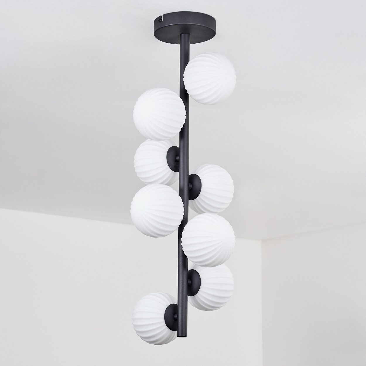 Eine moderne Deckenleuchte mit schwarzer Stange und acht weißen, kugelförmigen Lampen. Die Leuchte hängt an einer weißen Decke.