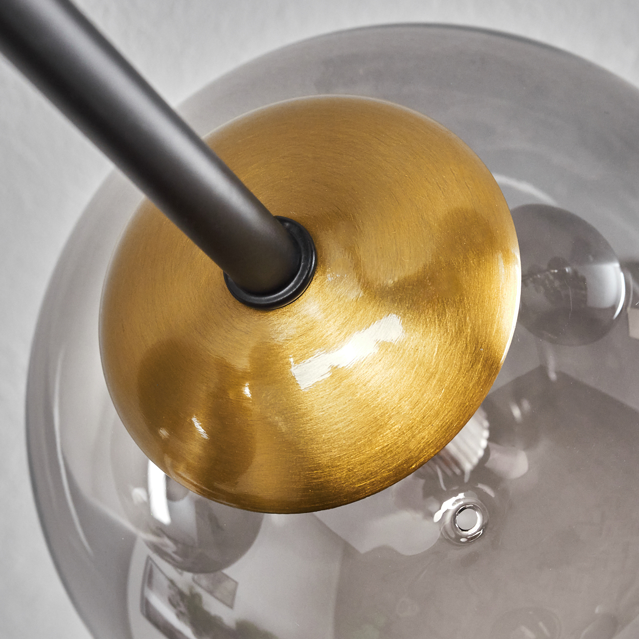 Nahaufnahme einer modernen Leuchte. Eine goldfarbene Kugel ist mit einem schwarzen Stab verbunden. Die Kugel befindet sich in einem grauen Glasglobus.