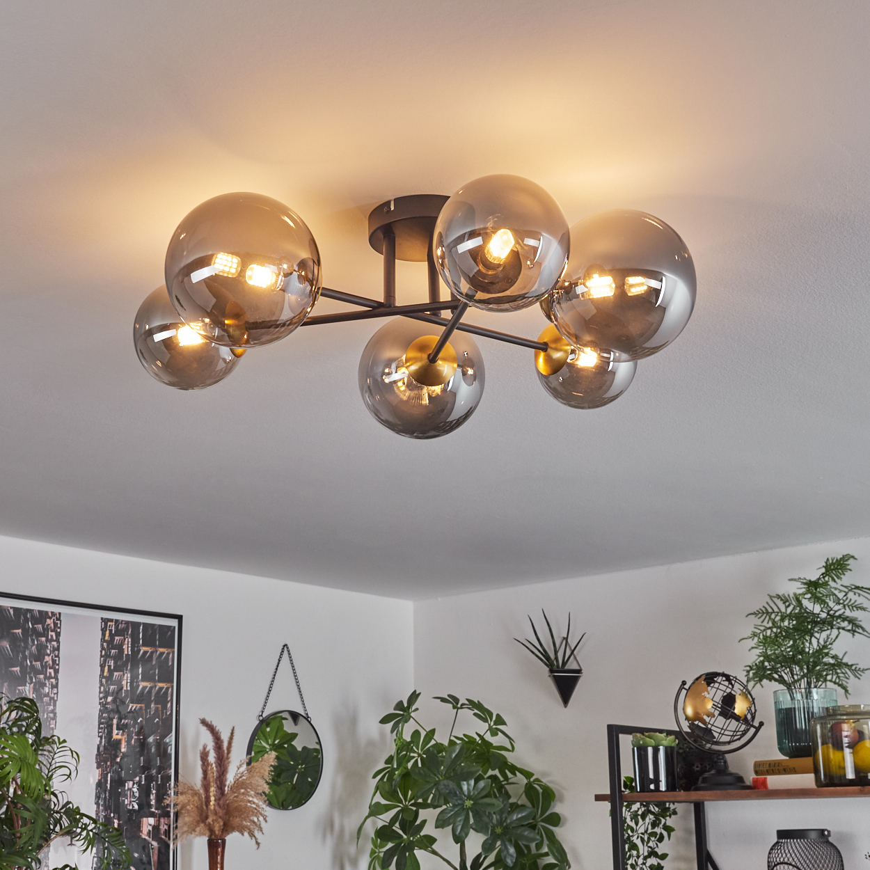 Eine moderne Deckenleuchte mit mehreren grauen Glaskugeln. Der Raum hat Pflanzen, einen Spiegel und ein Regal mit Dekoration.