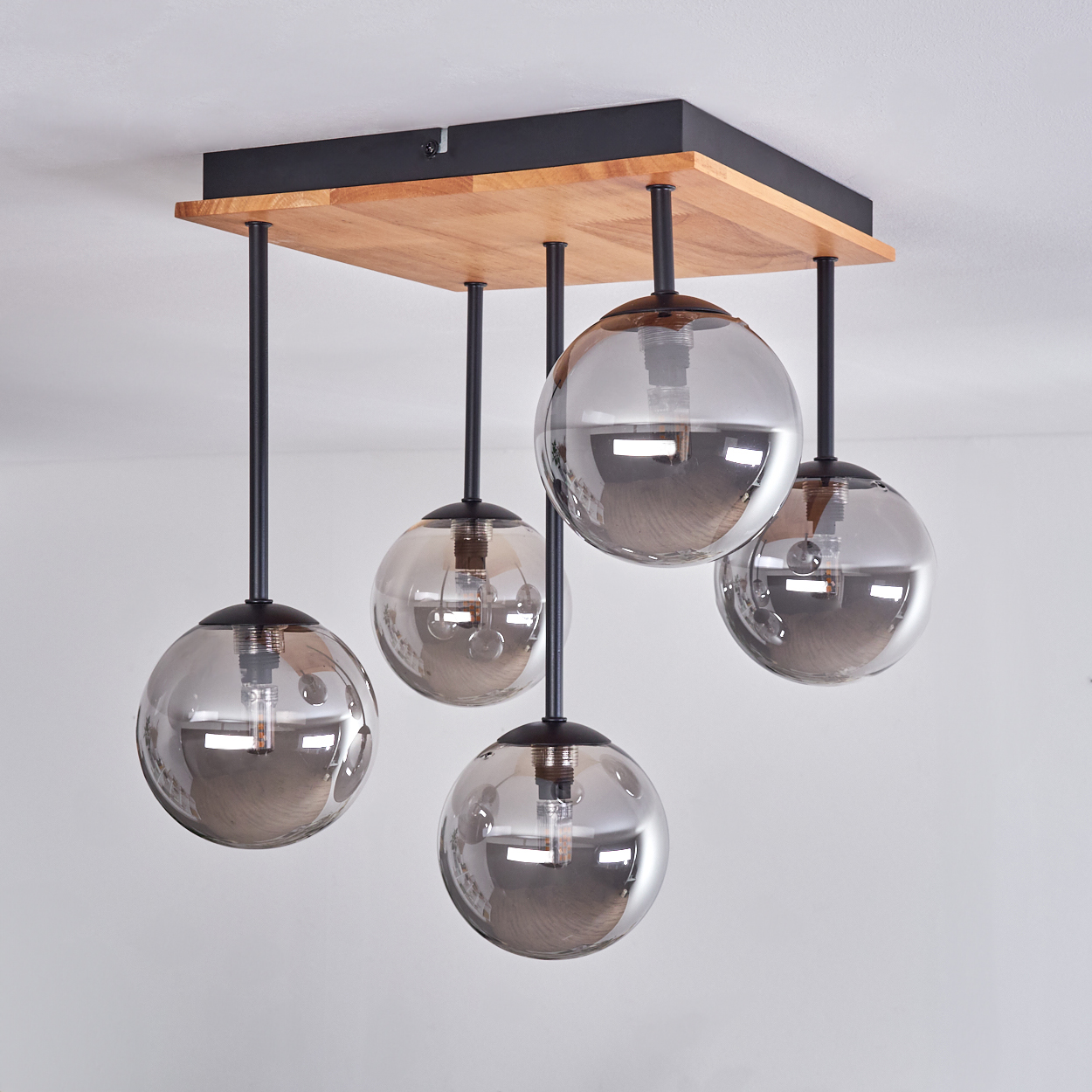 Eine moderne Leuchte mit fünf kugelförmigen Glasschirmen, die von einer quadratischen Basis aus Holz und schwarzem Metall hängen.