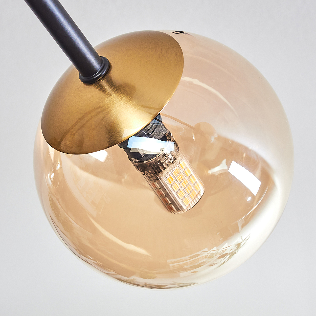 Nahaufnahme einer modernen Leuchte. Ein goldfarbener kreisförmiger Schirm bedeckt die Glühbirne in einer klaren, bernsteinfarbenen Glaskugel.