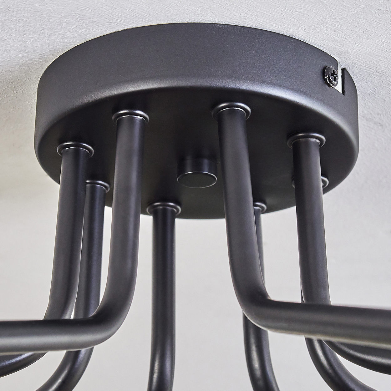 Nahaufnahme einer schwarzen Deckenleuchte. Sie hat eine kreisförmige Basis mit mehreren gebogenen Metallarmen, die nach unten verlaufen, an einer weißen Decke montiert.