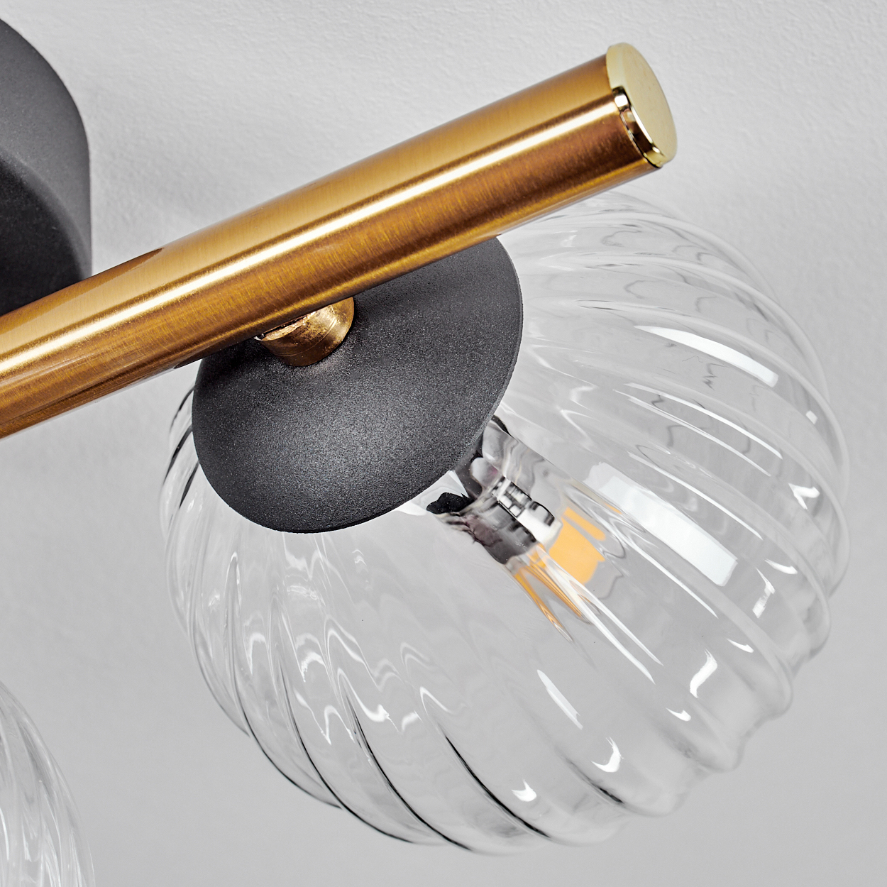Nahaufnahme einer modernen Leuchte. Sie hat einen goldenen Balken, einen schwarzen Sockel und einen klaren, geriffelten Glaskolben.