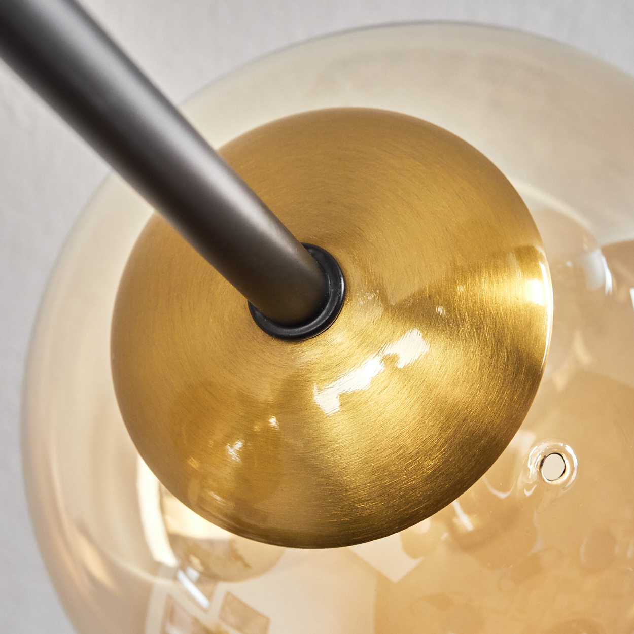 Nahaufnahme einer Lampe. Eine goldfarbene Scheibe ist zentriert, mit einer schwarzen Stange, die sich davon erstreckt. Im Hintergrund befindet sich eine Glaskugel.