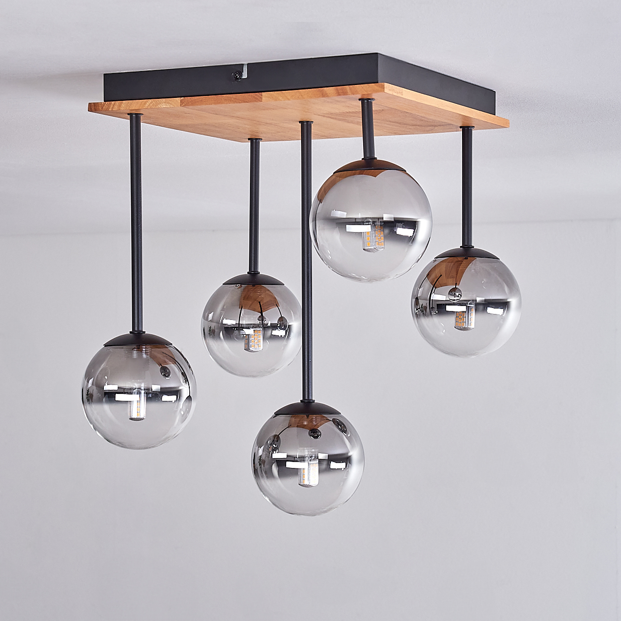 Eine moderne Deckenleuchte mit fünf Glasschirmen, die an einer quadratischen Holzbasis befestigt sind. Die Schirme sind klar mit reflektierender Oberfläche.