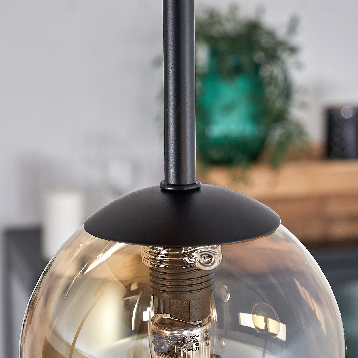 Nahaufnahme einer modernen Leuchte. Ein schwarzer Metallstab trägt eine Glaskugel. Im Inneren der Kugel ist eine Glühbirne sichtbar.