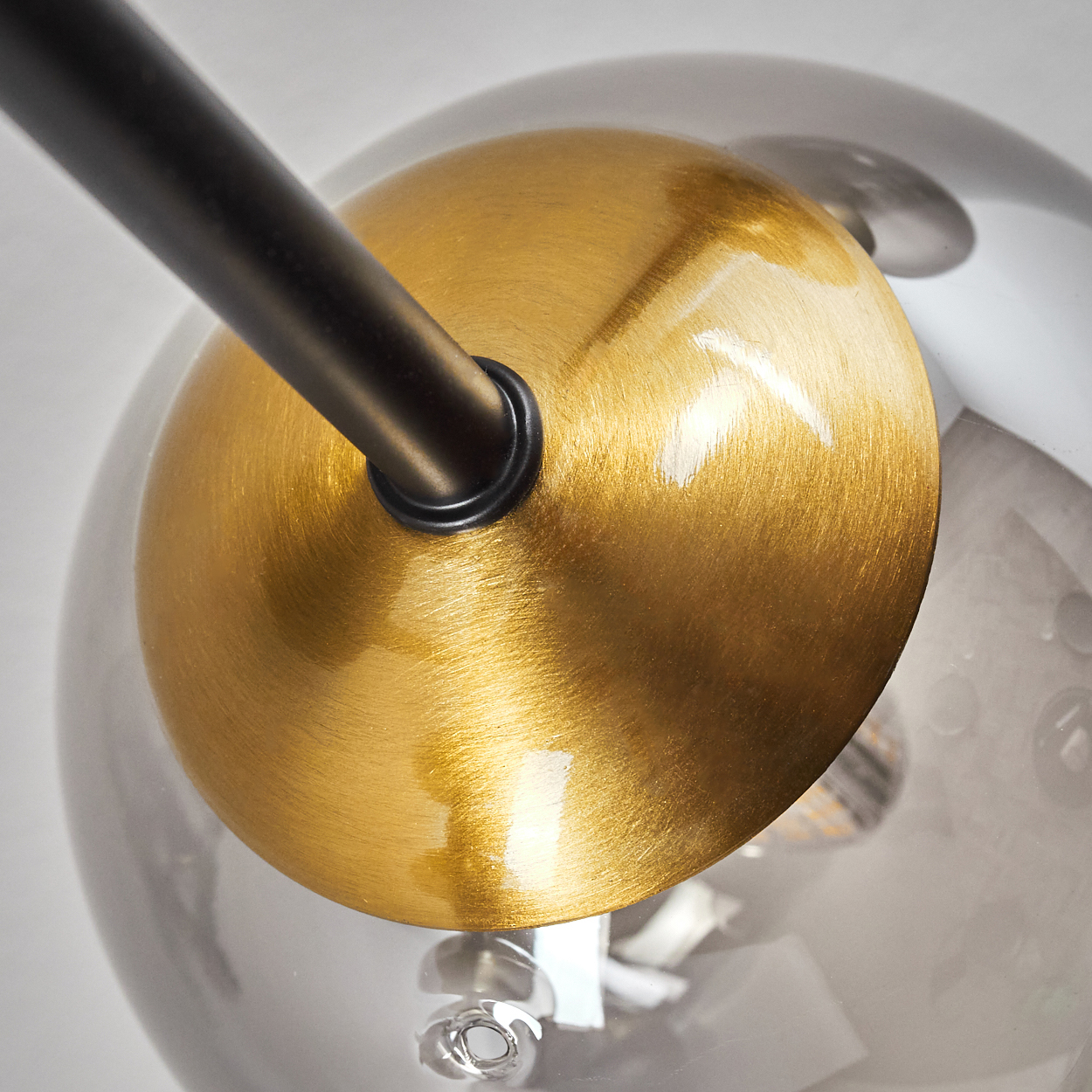 Nahaufnahme einer modernen Lampe. Eine schwarze Stange verbindet sich mit einer goldfarbenen Metallscheibe. Eine klare Glaskugel ist sichtbar.