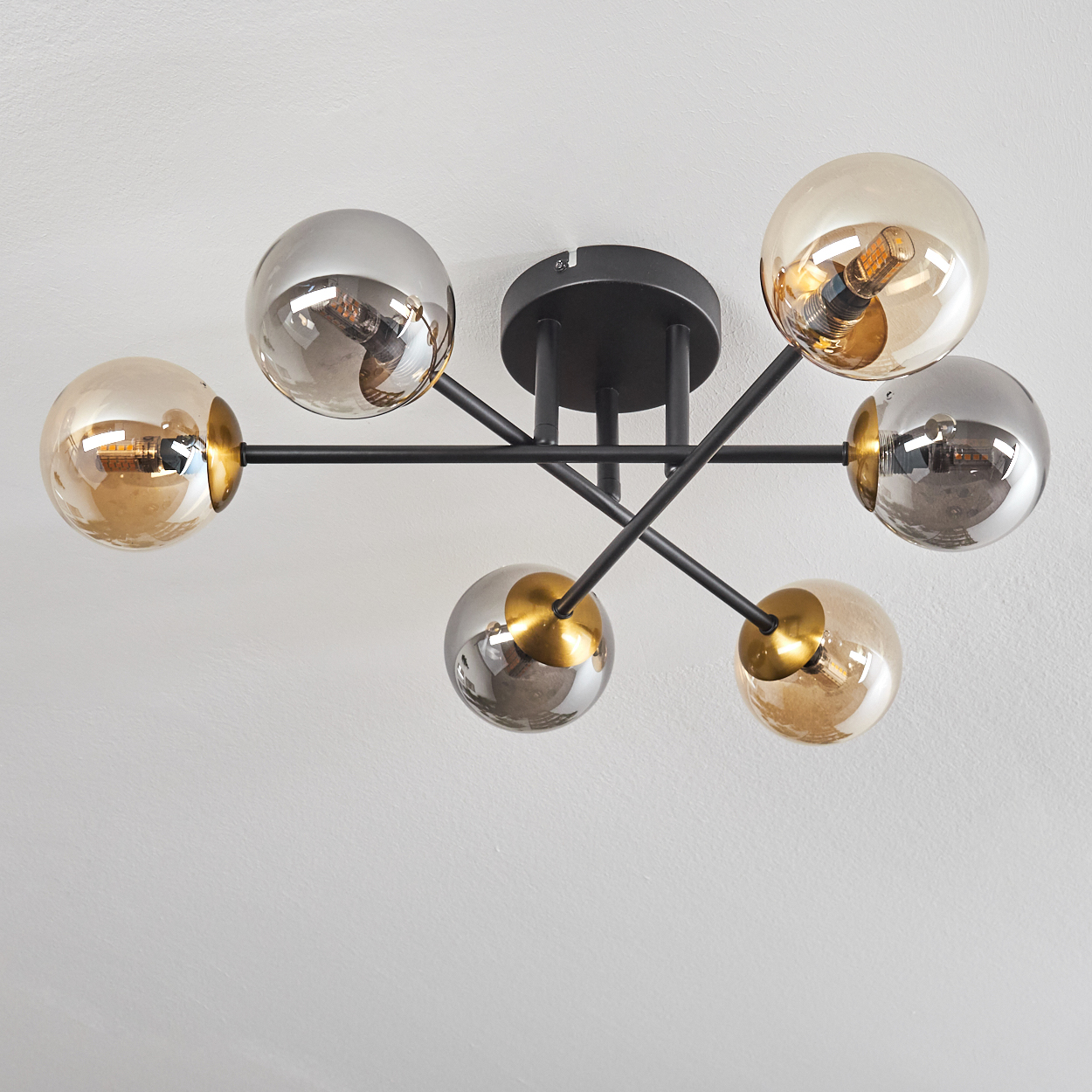 Eine Deckenleuchte mit sechs Glaskugeln in Gold und Silber, montiert auf schwarzen Metallarmen, vor einer weißen Decke.