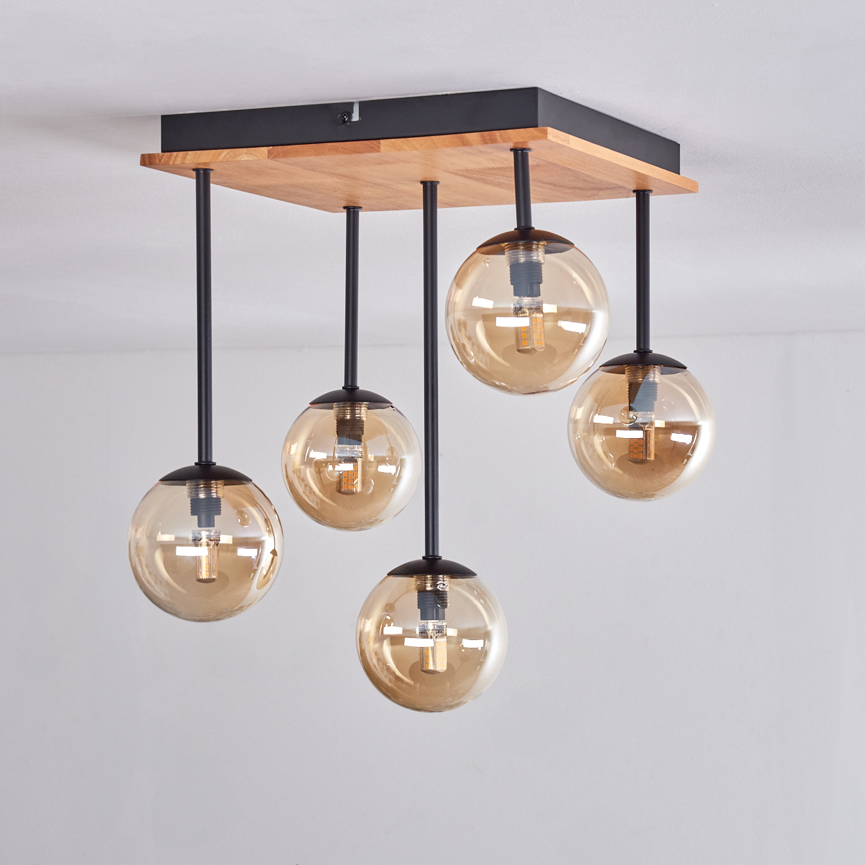 Eine Deckenlampe mit fünf bernsteinfarbenen Glaskugeln, die von einer Holz- und Metallhalterung hängen, vor weißem Hintergrund.