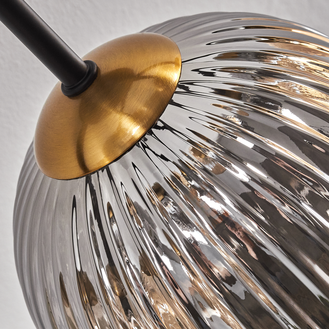 Nahaufnahme einer Lampe. Sie hat eine goldfarbene Oberseite mit einem schwarzen Stiel. Das Glas ist grau und geriffelt und reflektiert das Licht.