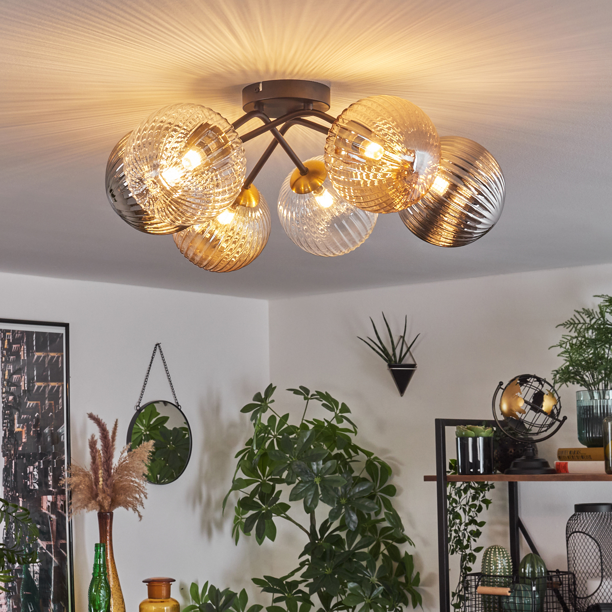 Eine Deckenlampe mit sechs Glaskugeln beleuchtet einen Raum mit Pflanzen und Dekorationen. Die Lampe ist der Mittelpunkt.