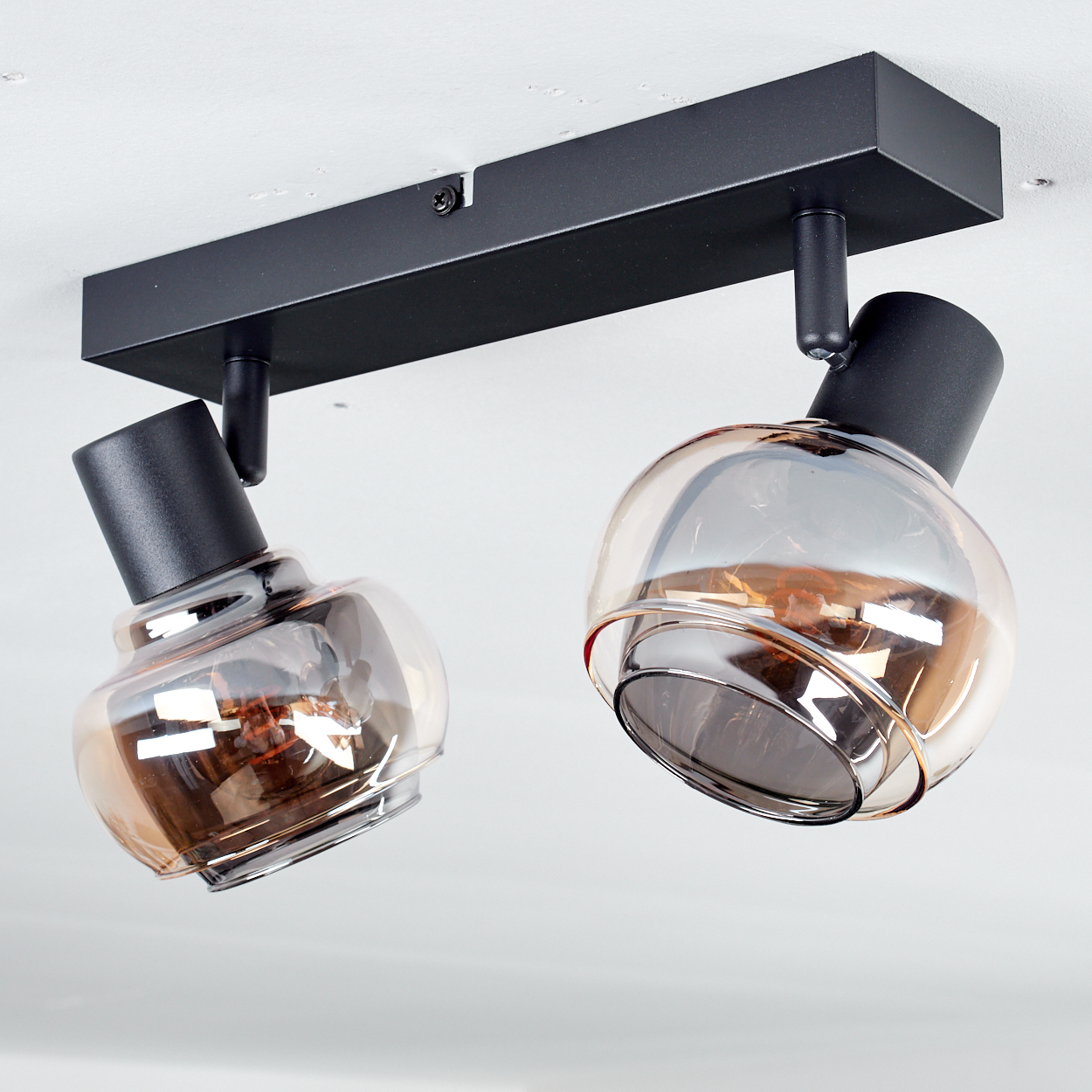 Zwei moderne Deckenstrahler. Jeder hat eine schwarze zylindrische Basis und einen klaren, gewölbten Glasschirm mit einer Glühbirne.