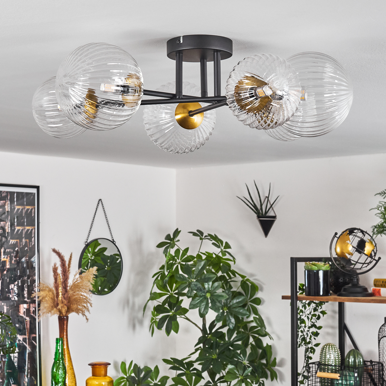 Moderne Deckenlampe mit Glaskugeln. Der Raum hat Pflanzen, einen Spiegel und Dekorationsgegenstände. Weiße Wände und eine helle Decke.