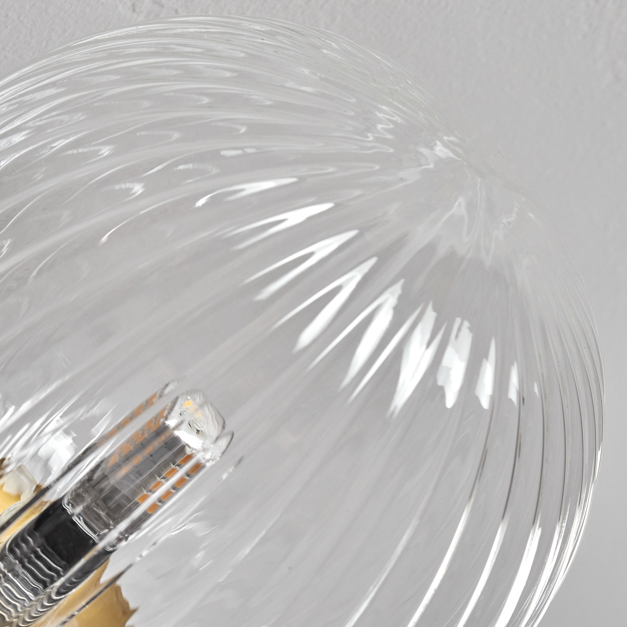 Nahaufnahme einer Glasleuchte. Sie hat ein klares, spiralförmiges Muster. Im Inneren ist eine kleine Glühbirne zu sehen.