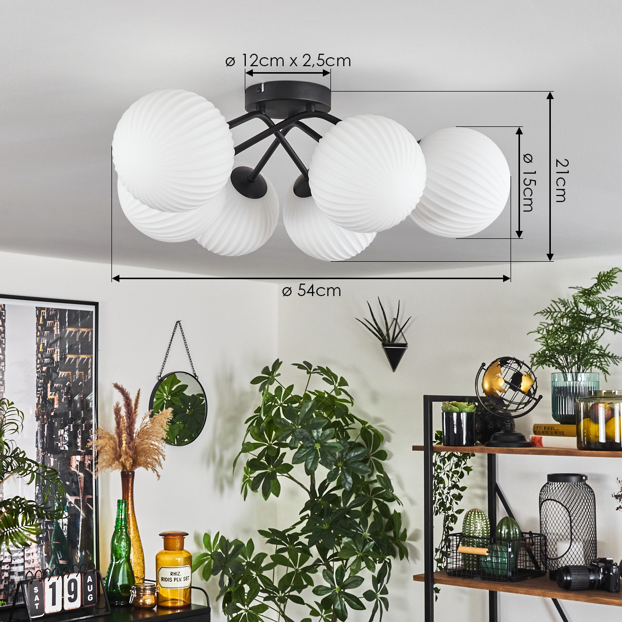 Eine weiße Deckenlampe mit schwarzen Armen ist an einer weißen Decke montiert. Der Raum ist mit Pflanzen und Regalen dekoriert.