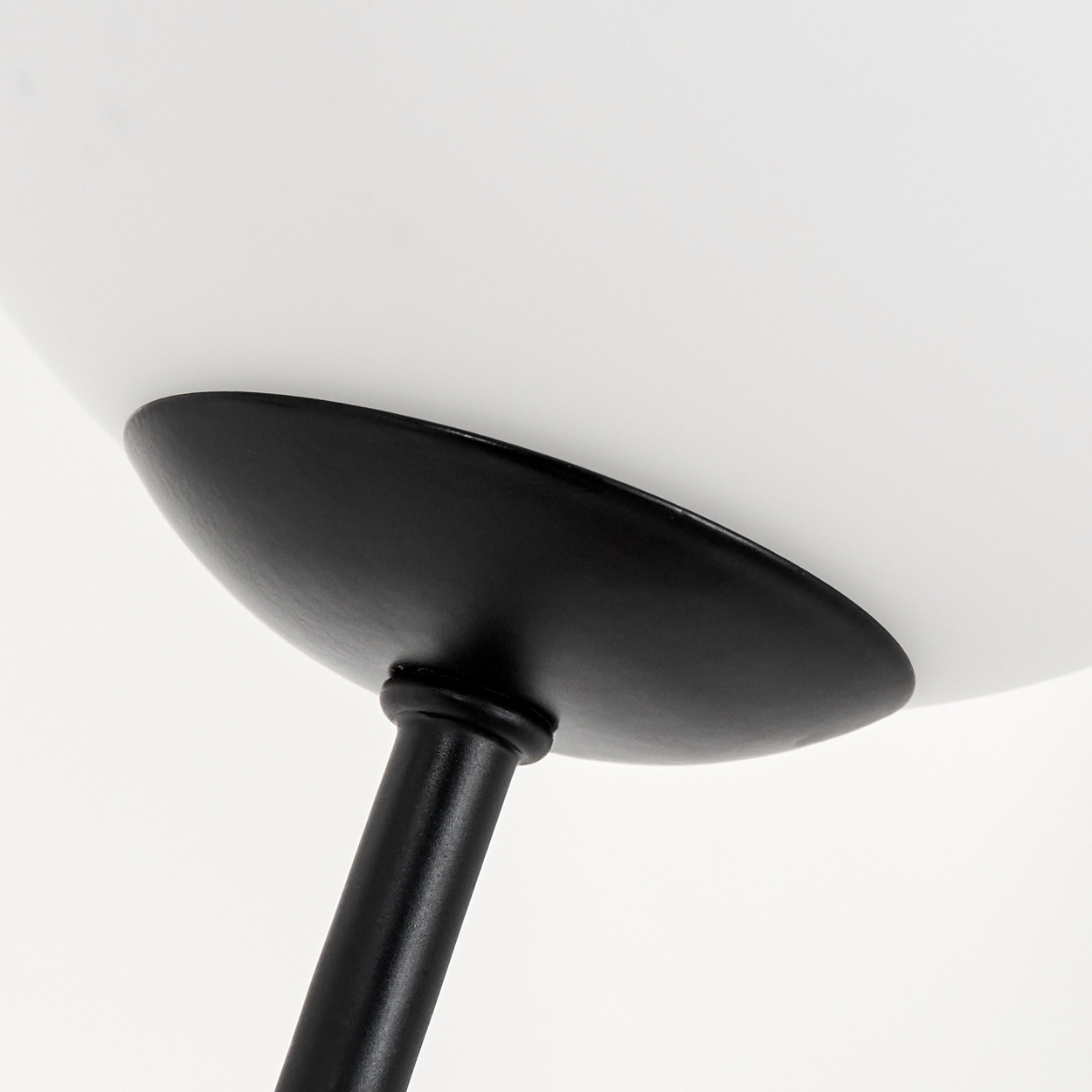 Nahaufnahme einer Lampe. Ein weißer Lampenschirm befindet sich über einem schwarzen, runden Sockel und Stiel, vor weißem Hintergrund.
