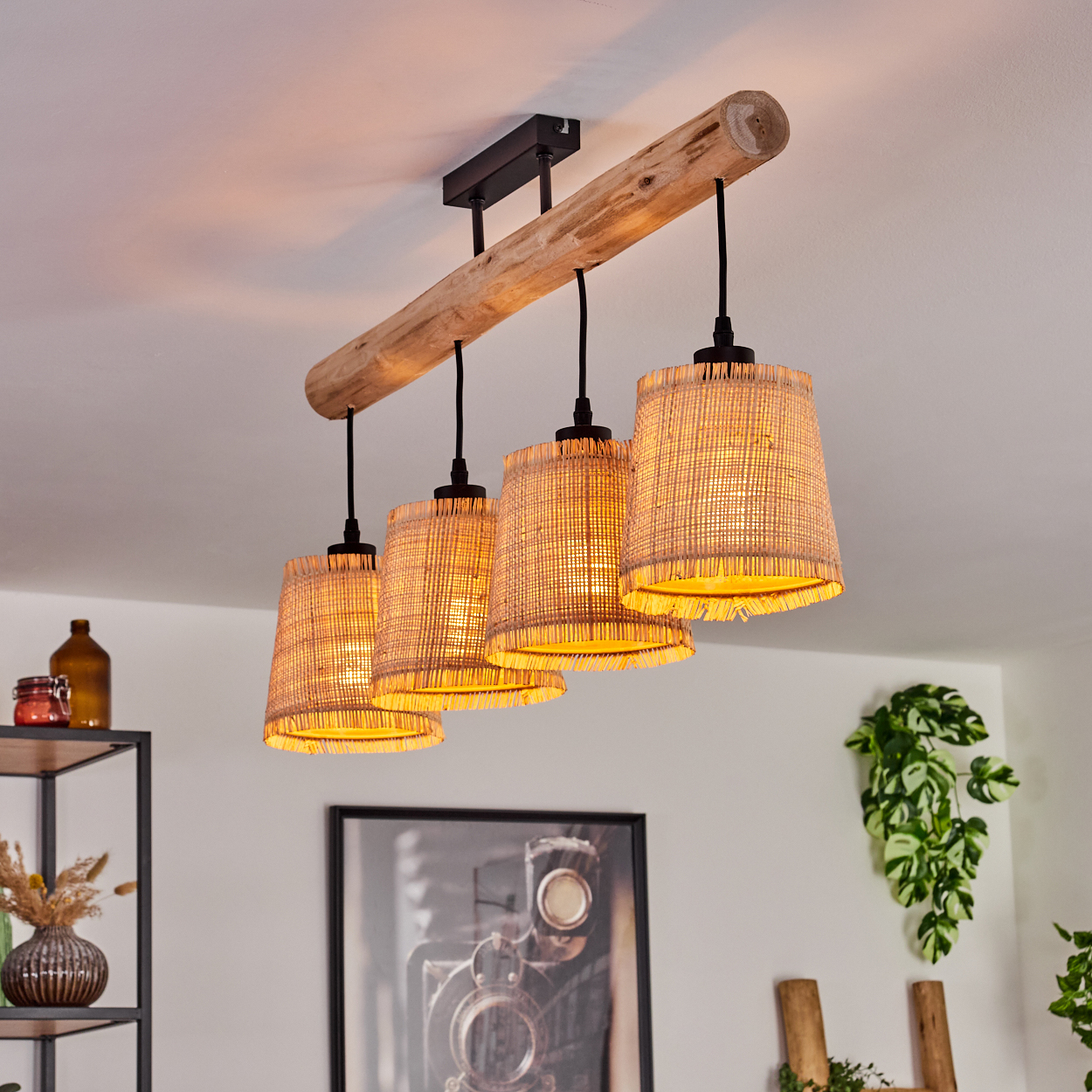 Ein Holzbalken mit vier gewebten Lampen hängt von einer weißen Decke. Ein schwarzer Rahmen mit einem Foto einer Kamera befindet sich darunter.