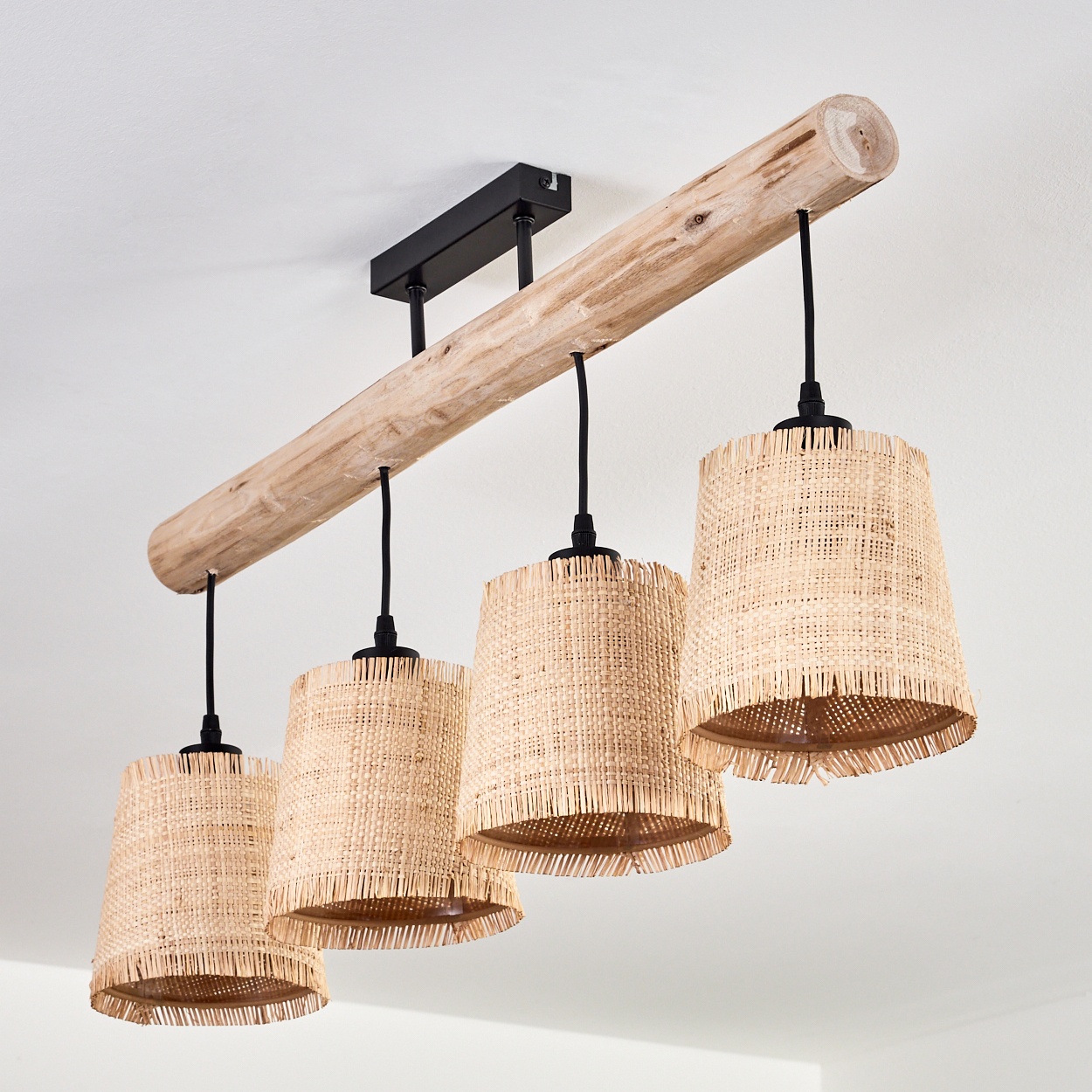 Ein Holzbalken mit vier gewebten Lampen hängt von einer weißen Decke. Schwarze Kabel verbinden Lampenschirme mit dem Balken, alle in einem natürlichen Ton.