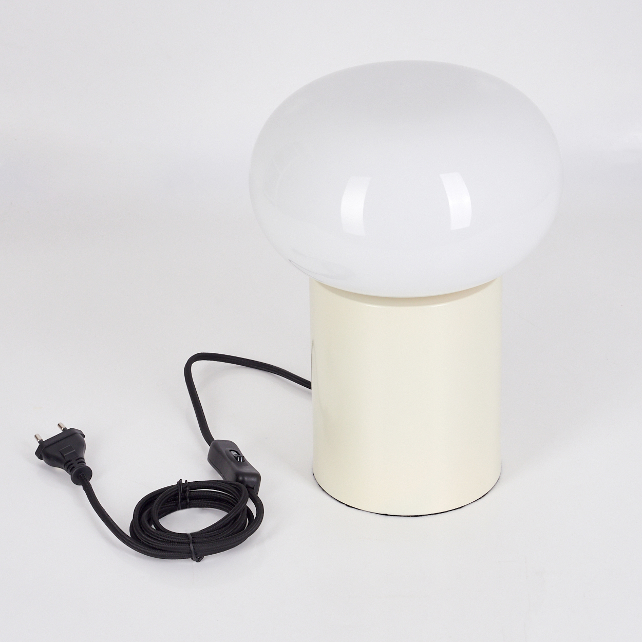 Eine pilzförmige Lampe mit weißem Oberteil und cremefarbenem Sockel. Ein schwarzes Netzkabel und Stecker sind sichtbar auf weißem Grund.