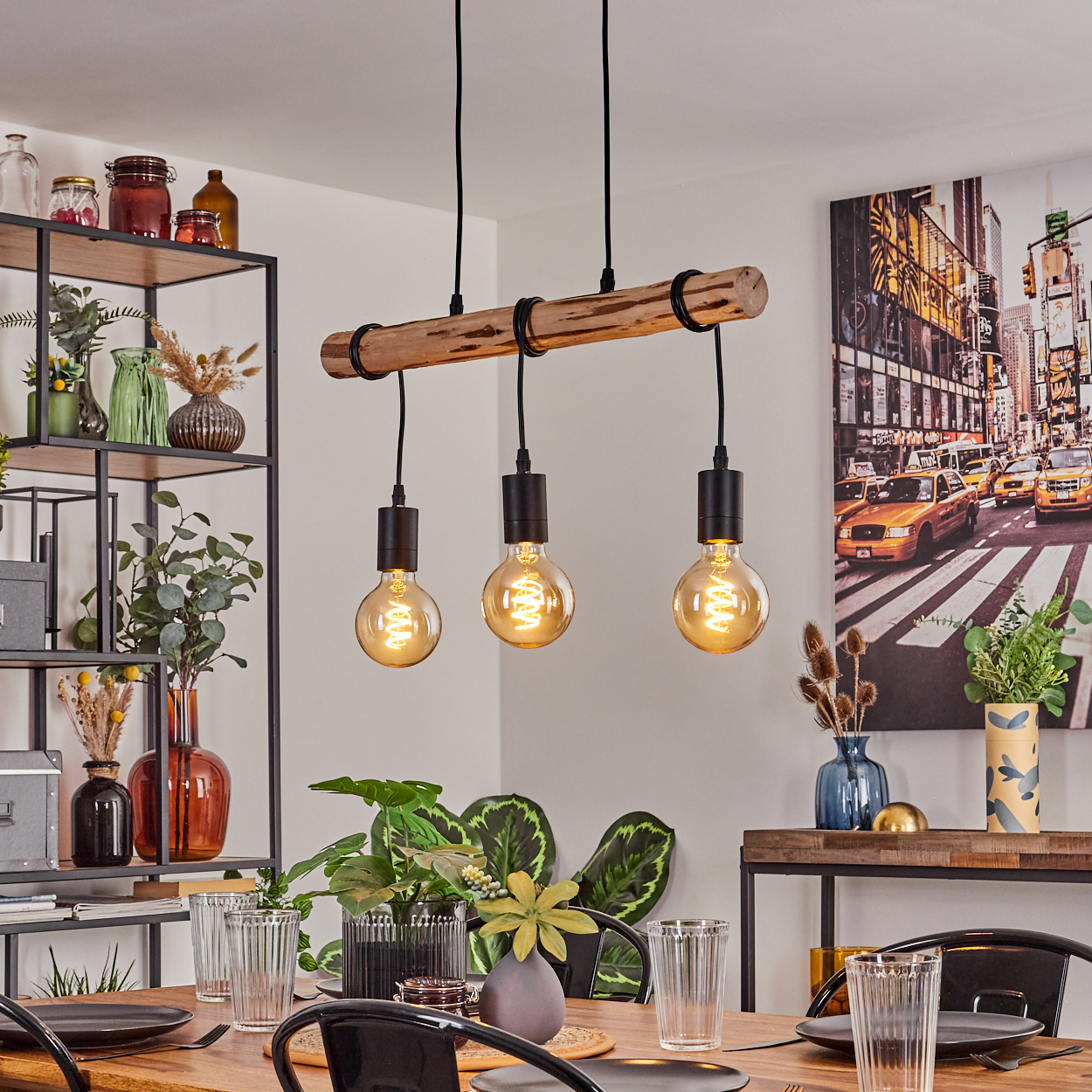 Esszimmer mit Holztisch, schwarzen Stühlen und drei Glühbirnen, die von einem Holzbalken hängen. New York Bild an der Wand.