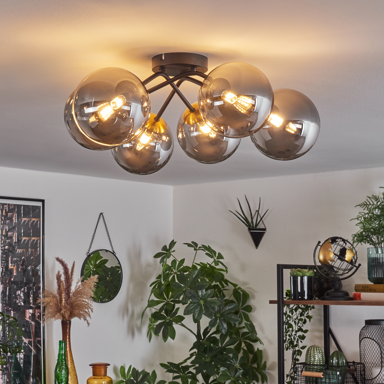 Deckenlampe mit sechs Glaskugeln. Pflanzen im Raum. Ein Spiegel an der Wand. Dekorationsartikel auf einem Regal. Heller und luftiger Raum.