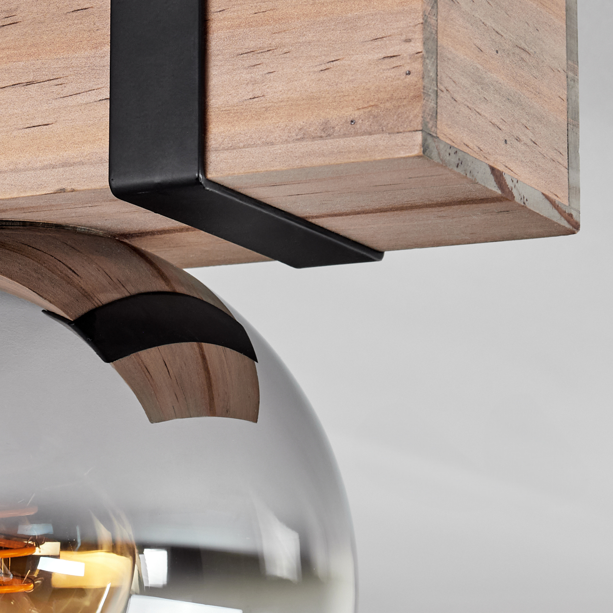 Nahaufnahme einer Holzlampenbefestigung. Ein Holzbalken wird von schwarzen Metallwinkeln gehalten, darunter eine Glaskugel.