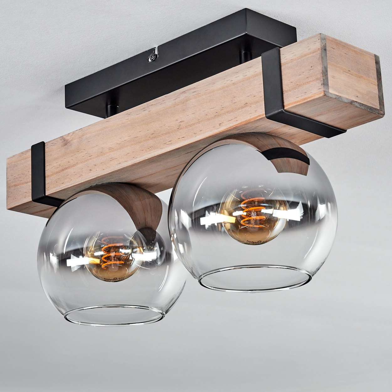 Eine Deckenleuchte mit zwei durchsichtigen Glaskugeln, Holzbalken, schwarzen Metallakzenten und sichtbaren Glühbirnen.