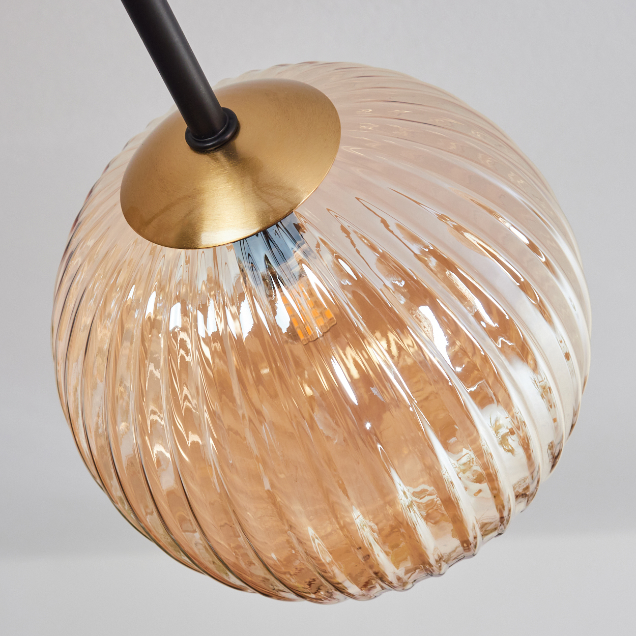 Nahaufnahme einer Glaslampe. Die Lampe hat einen runden, geriffelten, bernsteinfarbenen Schirm, eine Messingkappe und einen schwarzen Stiel vor weißem Hintergrund.