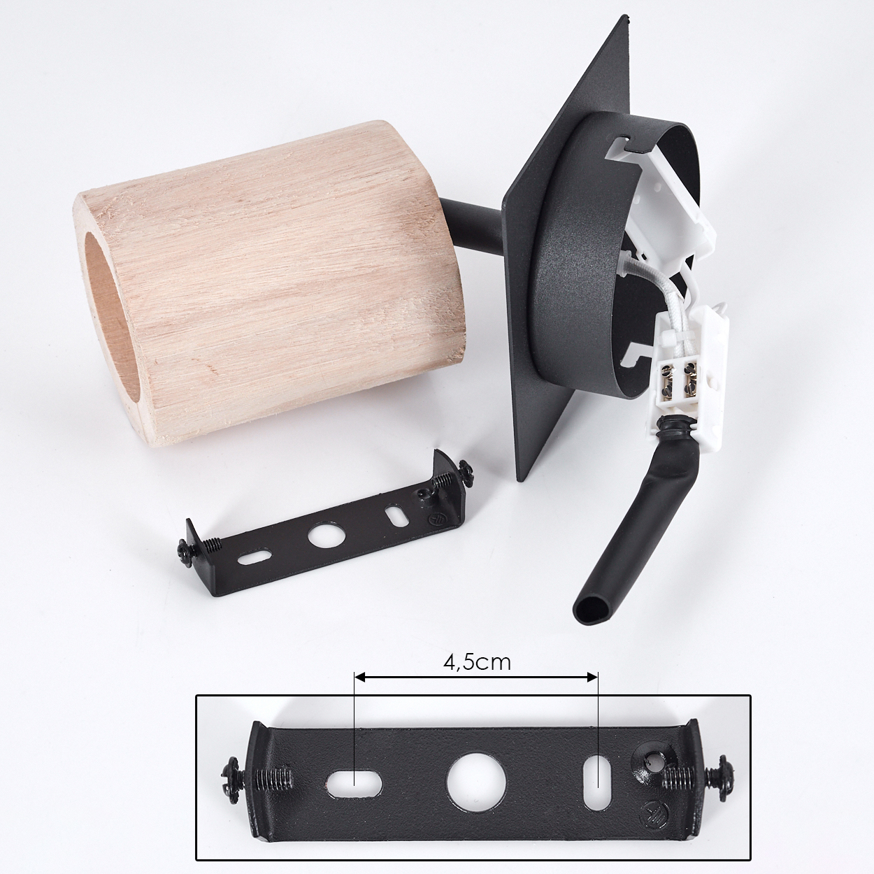 Eine zerlegte Lampe mit Holzzylinder, schwarzen Metallteilen und einer weißen elektrischen Komponente auf weißem Untergrund.