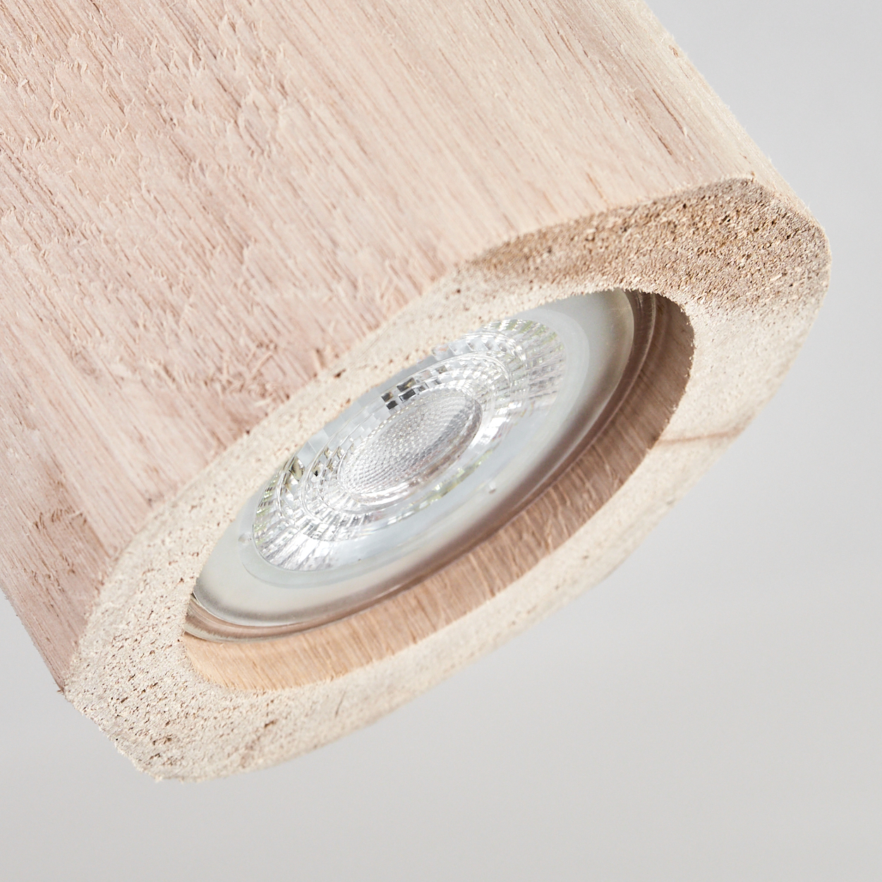 Nahaufnahme einer Holzleuchte mit einer hellen, kreisförmigen LED. Das Holz ist hellbraun, der Hintergrund ist weiß.