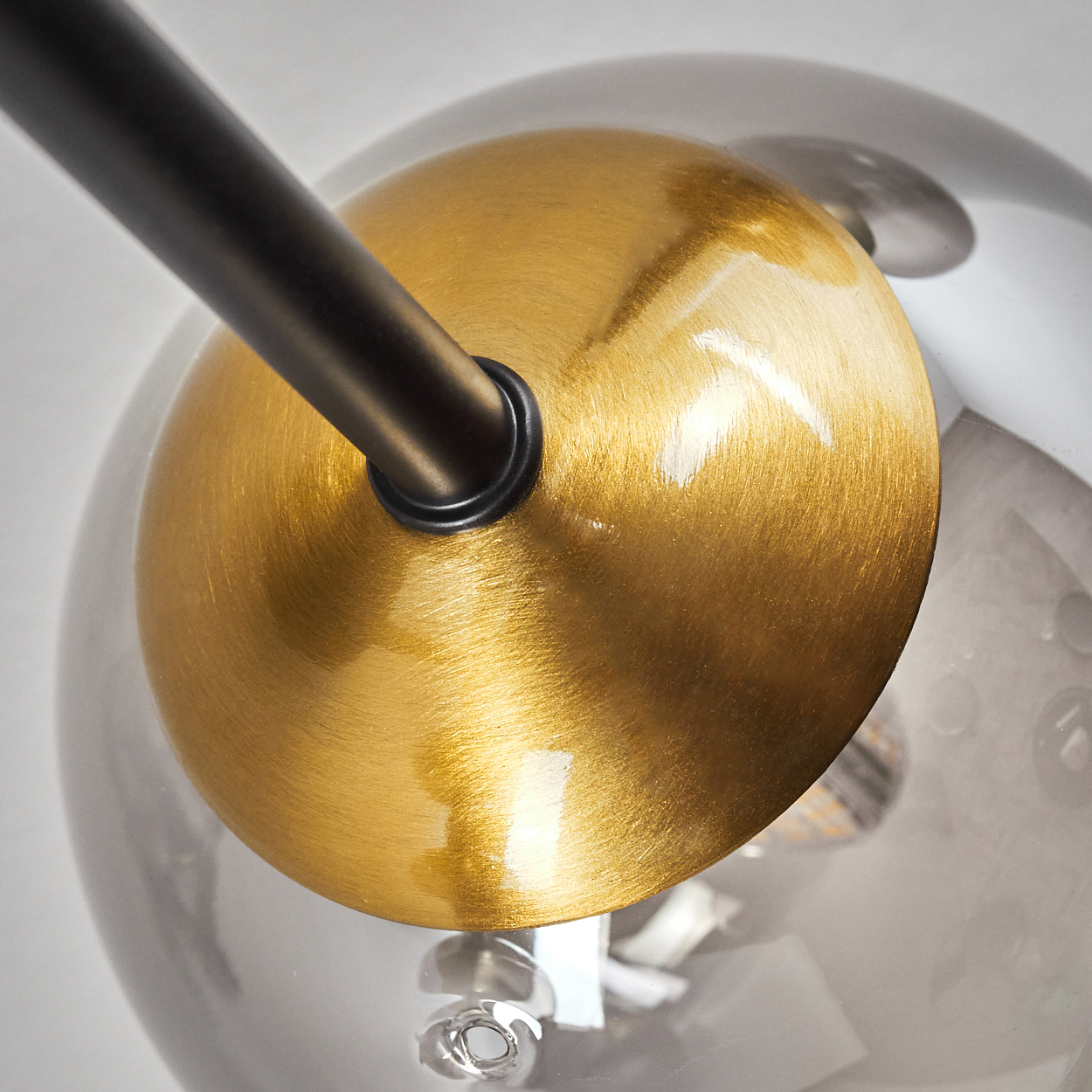 Nahaufnahme einer modernen Lampe. Eine messingfarbene Scheibe bedeckt eine klare Glaskugel, mit einem schwarzen Metallarm. Der Hintergrund ist weiß.