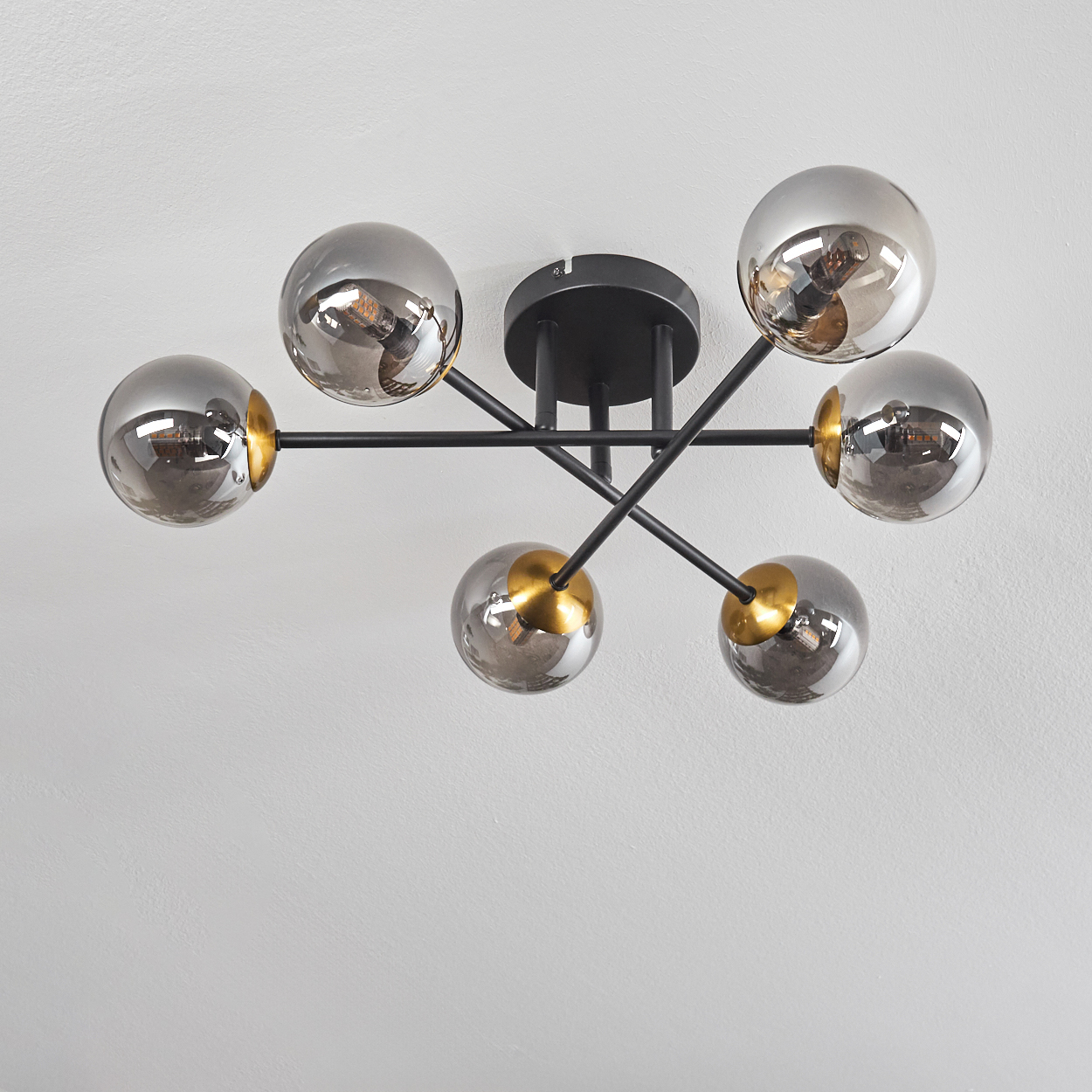Eine moderne Deckenleuchte. Sie hat sechs kugelförmige, verspiegelte Glasschirme, die an schwarzen Armen befestigt sind, mit goldenen Akzenten, an einer weißen Decke.