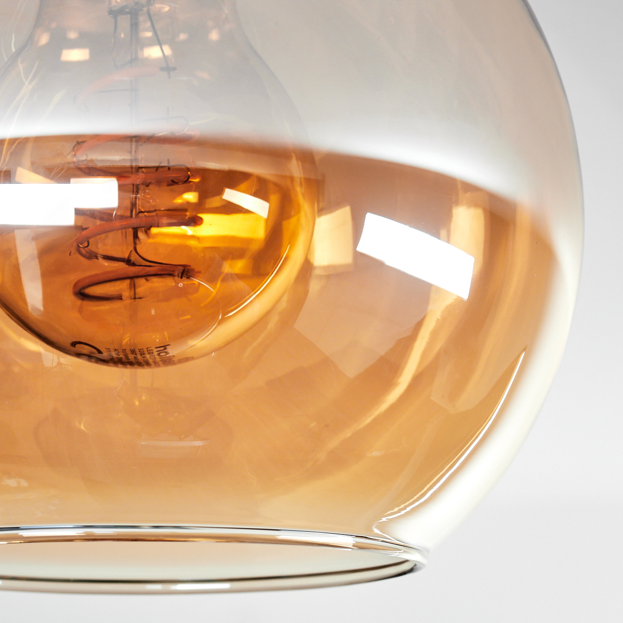 Nahaufnahme einer Leuchte. Ein transparenter Glasschirm umgibt eine leuchtende, bernsteinfarbene Glühbirne.