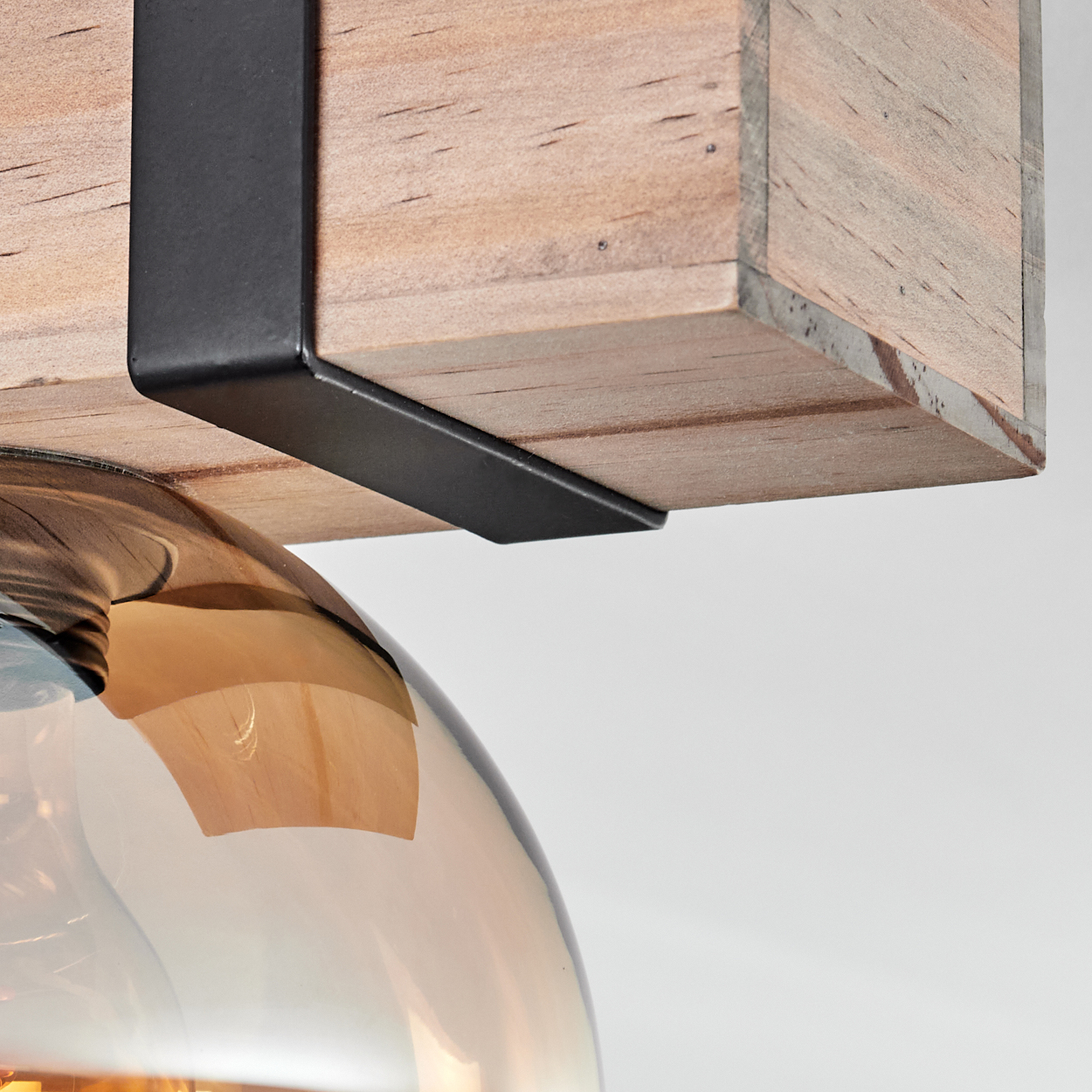 Nahaufnahme einer Leuchte. Ein Holzbalken wird von einer schwarzen Metallhalterung gehalten. Unterhalb befindet sich eine braune Glühbirne.