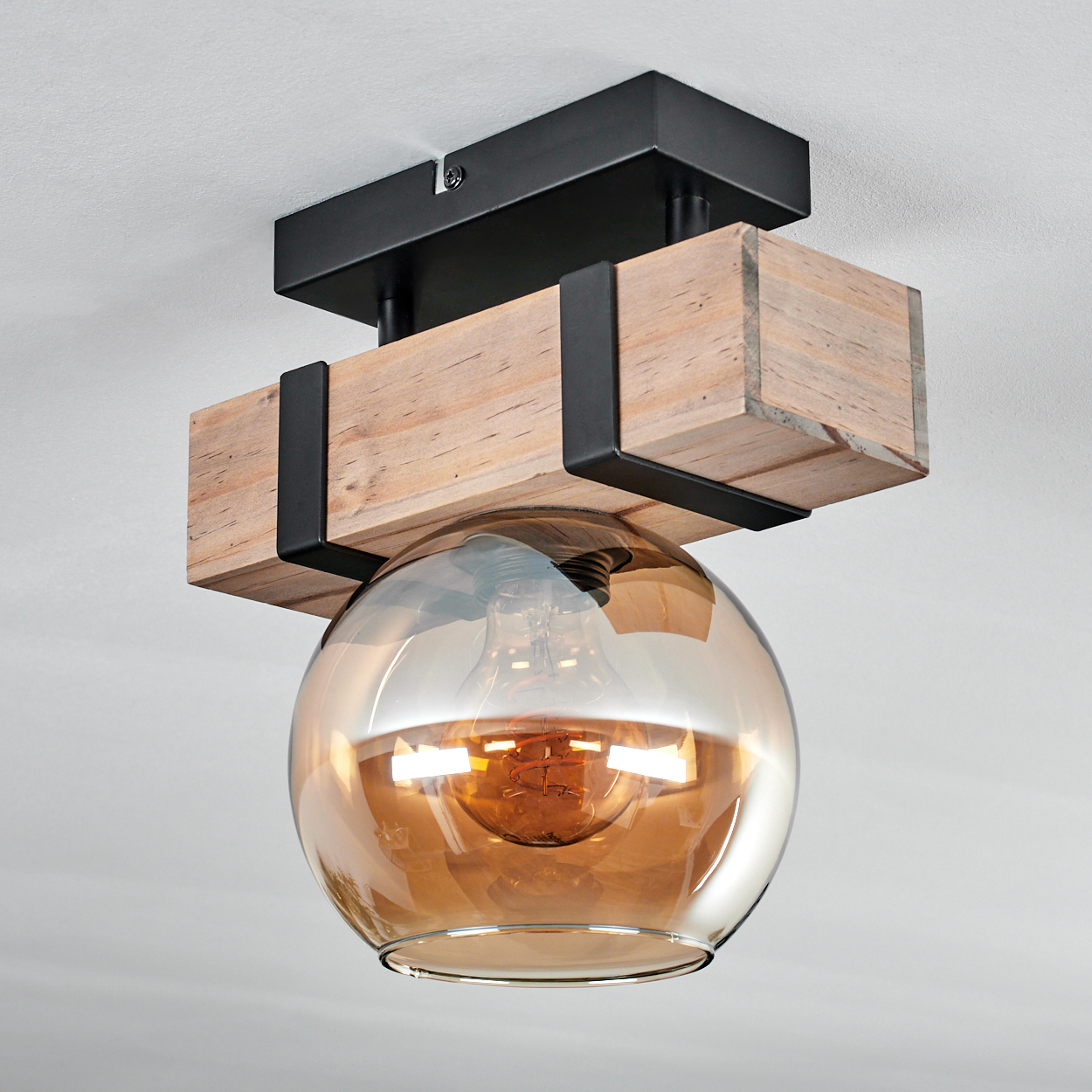 Deckenleuchte mit Holzbalken, schwarzen Metallakzenten und einem kugelförmigen bernsteinfarbenen Glasschirm.