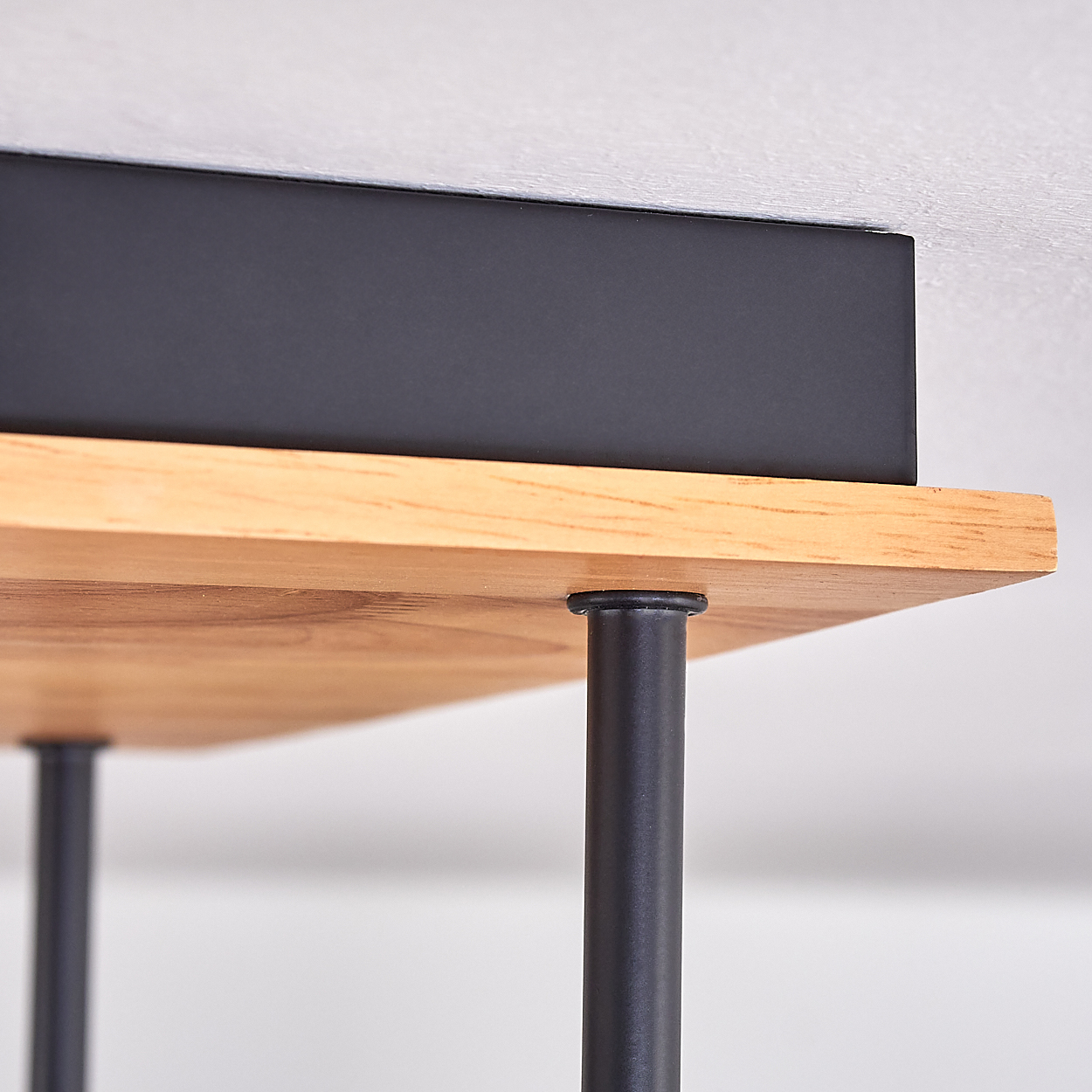 Nahaufnahme eines Holzregals mit schwarzen Metallbeinen. Auf dem Regal steht eine schwarze Box. Weiße Wand im Hintergrund.