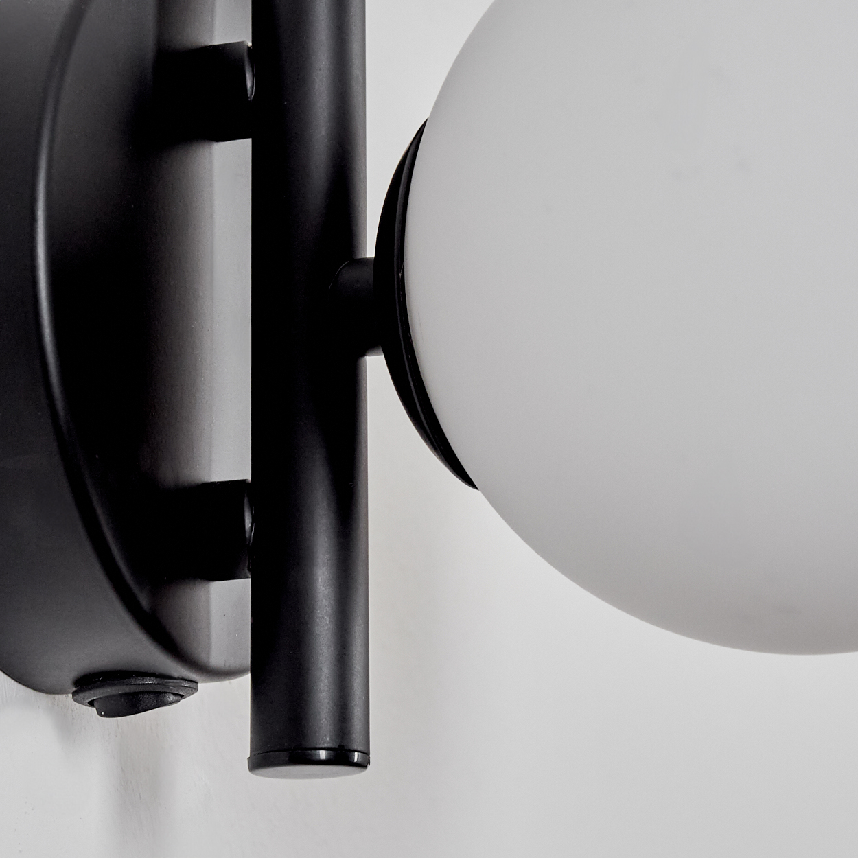 Nahaufnahme einer schwarzen Wandleuchte mit rundem, weißem Glasschirm. Die Lampe ist an einer weißen Wand montiert.