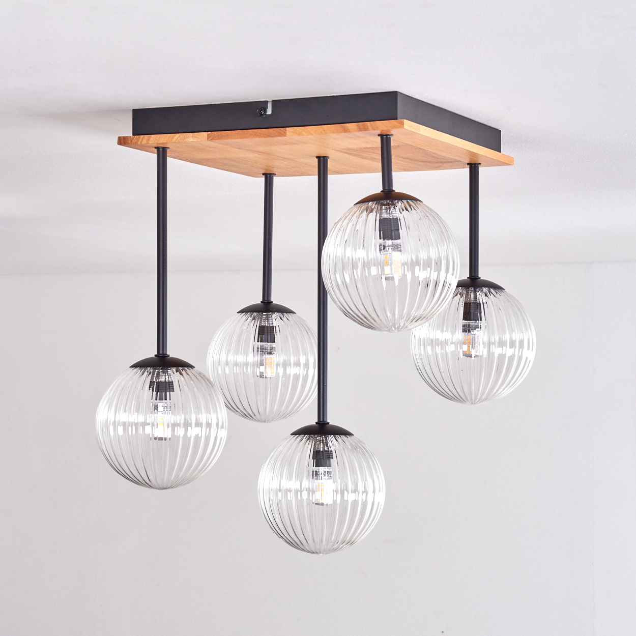 Ein moderner Kronleuchter mit fünf klaren, gerippten Glaskugellampen hängt von einer Holz- und schwarzen Metallbefestigung.
