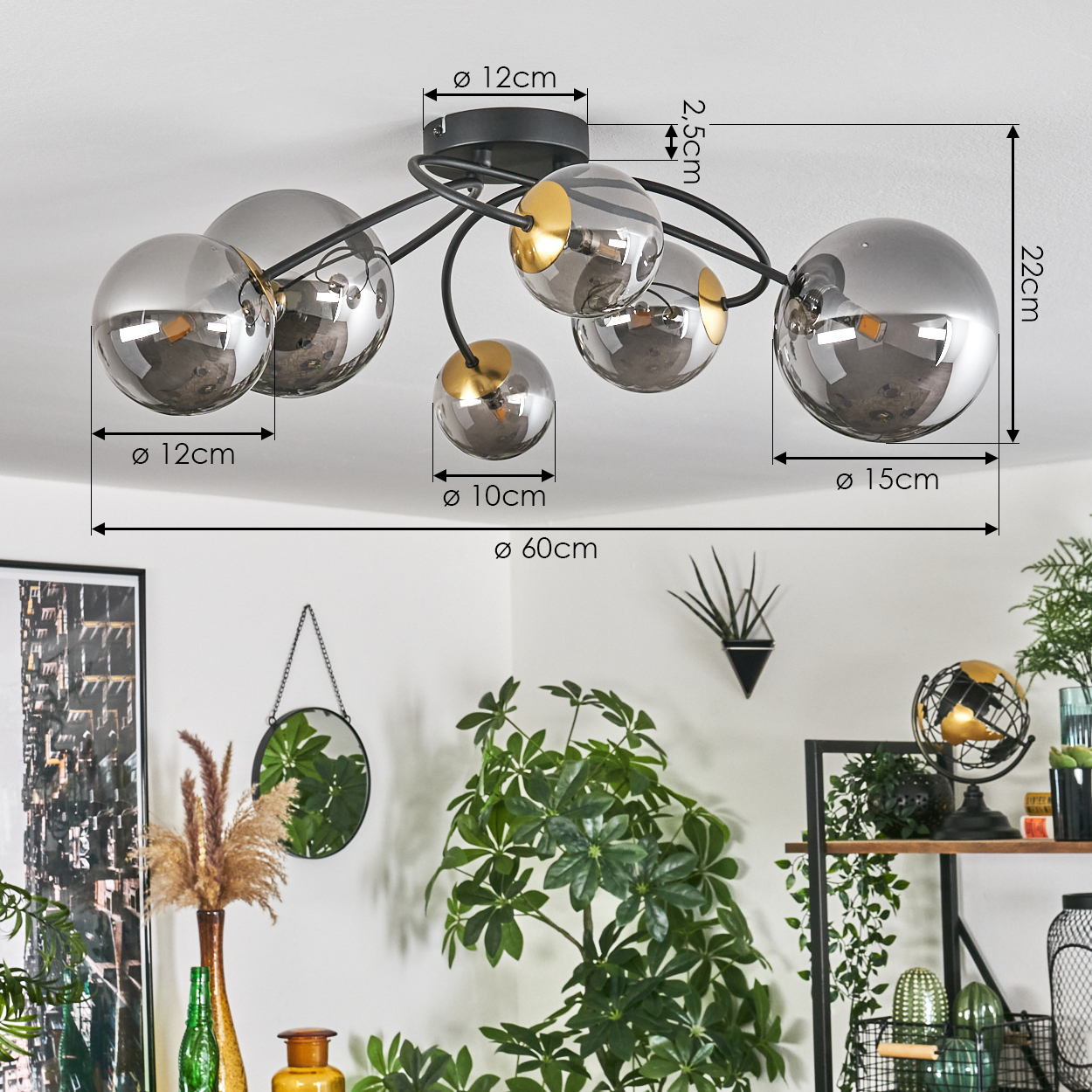 Eine Deckenleuchte mit sechs grauen Glaskugelschirmen. Die Leuchte hat schwarze Metallarme. Im Hintergrund befinden sich Dekorationen mit Pflanzen und Regalen.